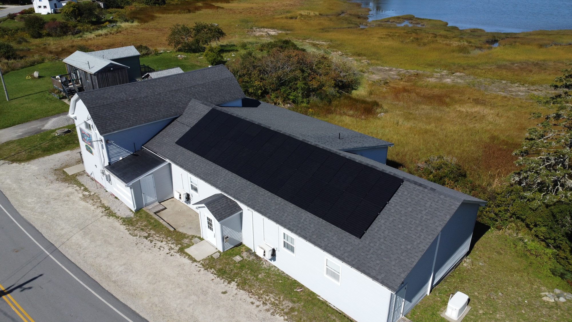 Aerial view of a community hall on Surettes Island, Nova Scotia with a 14 kW solar array and salt marsh behind